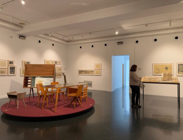 Sala de la exposición con mobiliario sobre una tarima circular y planos en las paredes