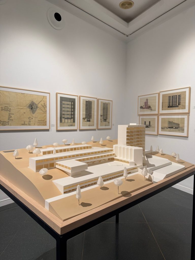 Maqueta expuesta en la sala, con planos enmarcados al fondo